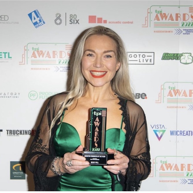 Smiling blonde woman in green dress (Becky Pell) holding monitor engineer of the year award from tpi awards.